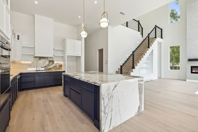 kitchen with tasteful backsplash, light hardwood / wood-style flooring, white cabinets, a kitchen island, and hanging light fixtures