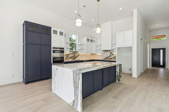 kitchen with a large island, hanging light fixtures, light stone counters, light hardwood / wood-style flooring, and white cabinets