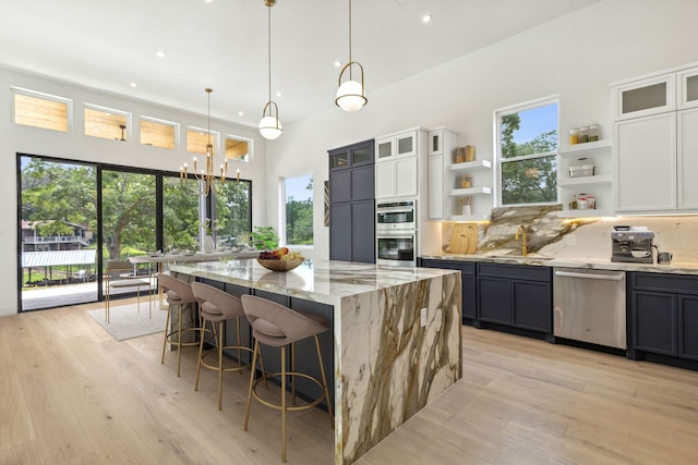 kitchen featuring pendant lighting, a center island, light stone countertops, appliances with stainless steel finishes, and white cabinetry