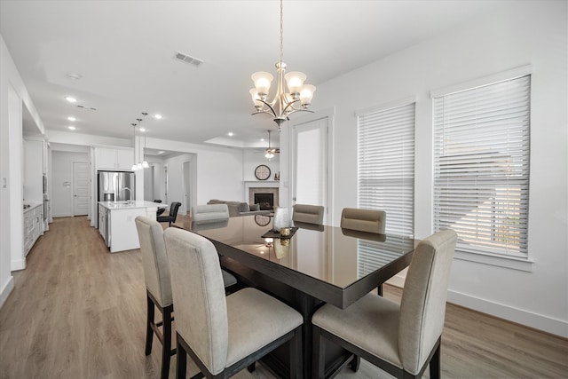 dining room with light wood finished floors, baseboards, visible vents, a fireplace, and a notable chandelier