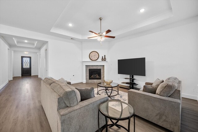 living area featuring ceiling fan, a fireplace, wood finished floors, baseboards, and a tray ceiling