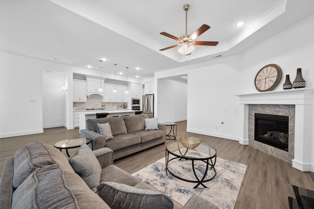 living room with a raised ceiling, visible vents, light wood-type flooring, baseboards, and a tile fireplace