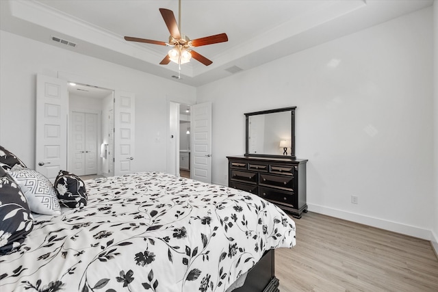 bedroom featuring a tray ceiling, visible vents, light wood-style floors, a ceiling fan, and baseboards