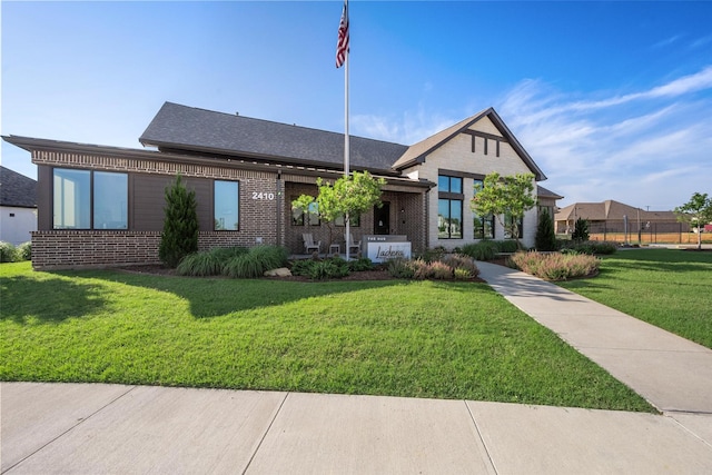 view of front facade featuring brick siding, a front yard, fence, and a shingled roof