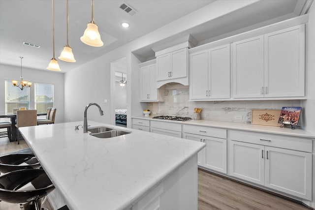 kitchen featuring light wood finished floors, tasteful backsplash, visible vents, white cabinets, and a sink