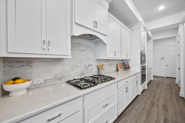 kitchen featuring tasteful backsplash, light stone counters, appliances with stainless steel finishes, wood finished floors, and white cabinetry