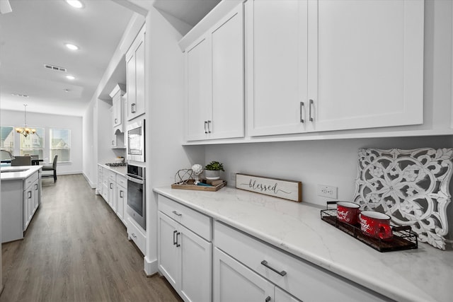 kitchen with visible vents, appliances with stainless steel finishes, white cabinetry, a sink, and wood finished floors