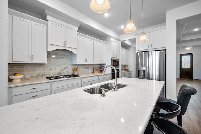 kitchen with stainless steel appliances, wood finished floors, a sink, decorative backsplash, and light stone countertops