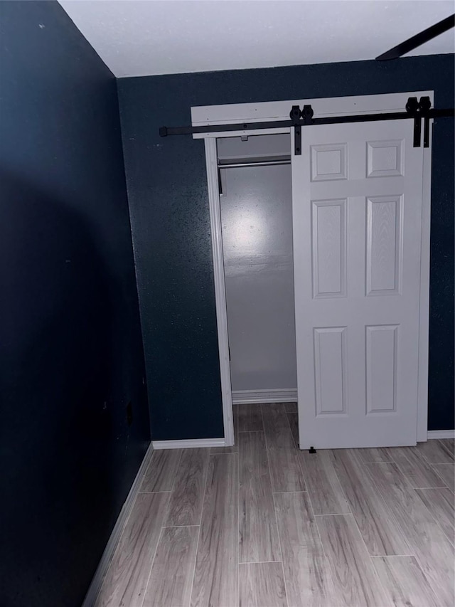 unfurnished bedroom with light wood-type flooring, a barn door, and a closet