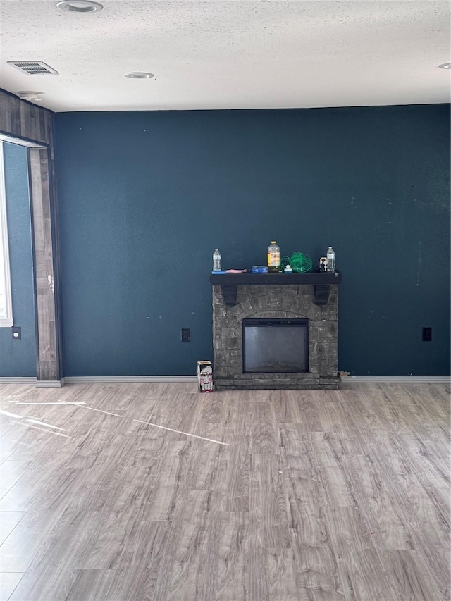 unfurnished living room featuring a textured ceiling, hardwood / wood-style floors, and a stone fireplace