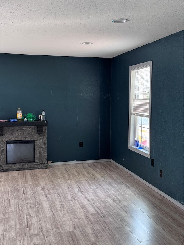 unfurnished living room with a textured ceiling, light wood-type flooring, and a stone fireplace