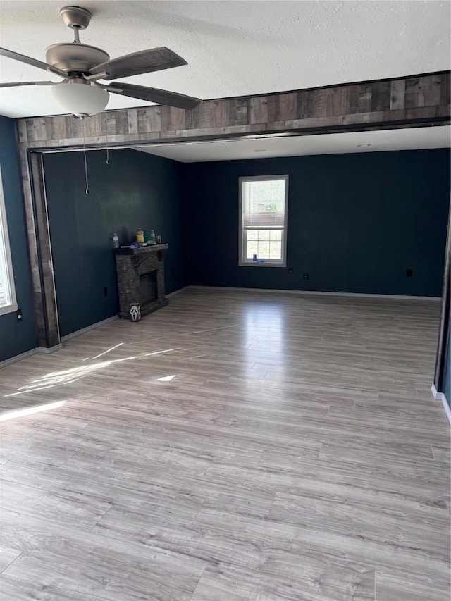 empty room featuring a fireplace, a textured ceiling, ceiling fan, and light wood-type flooring