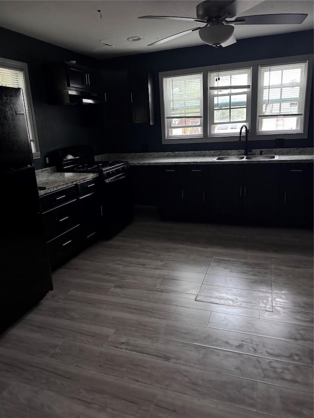 kitchen featuring black appliances, light stone countertops, ceiling fan, hardwood / wood-style flooring, and sink