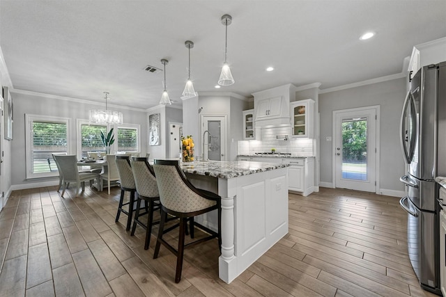 kitchen featuring stainless steel fridge, backsplash, white cabinets, a center island, and light stone counters