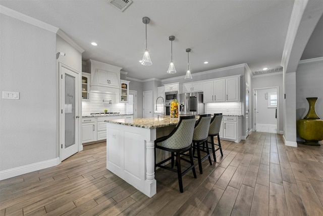 kitchen with stainless steel appliances, light stone counters, a kitchen island with sink, white cabinets, and hardwood / wood-style flooring