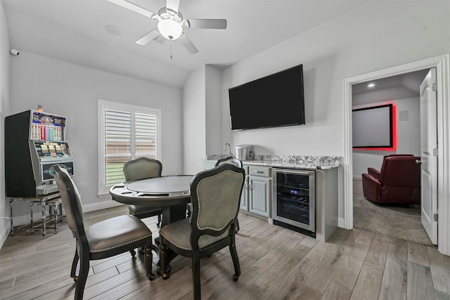 dining room with ceiling fan, wine cooler, light hardwood / wood-style floors, vaulted ceiling, and indoor bar