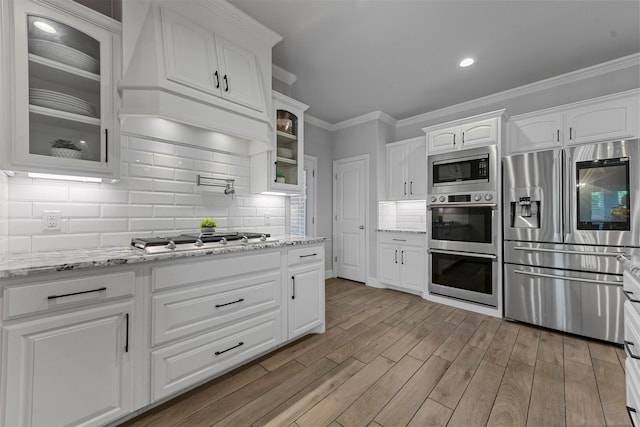 kitchen featuring stainless steel appliances, light stone counters, light hardwood / wood-style flooring, decorative backsplash, and white cabinets