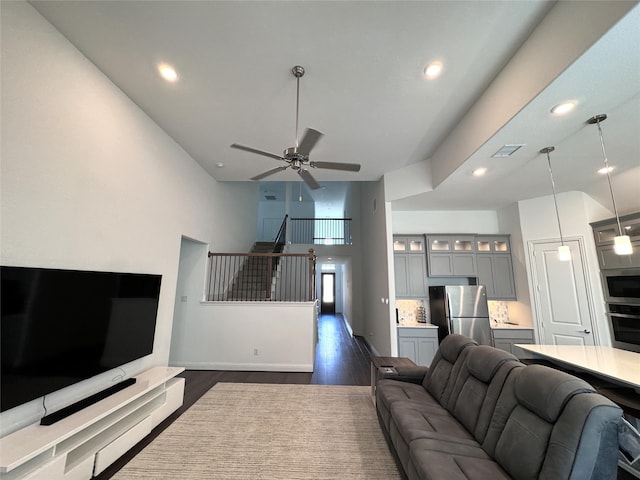 living room featuring dark hardwood / wood-style flooring, ceiling fan, and a high ceiling