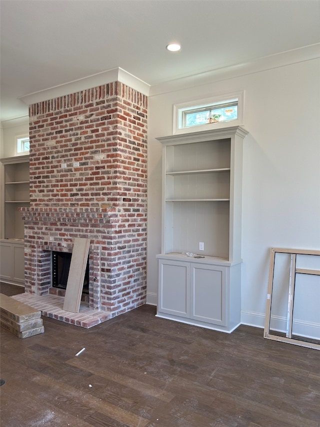 unfurnished living room with built in shelves, crown molding, baseboards, a fireplace, and wood finished floors