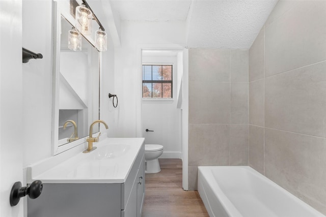 bathroom featuring vanity, a textured ceiling, a bath, wood-type flooring, and toilet