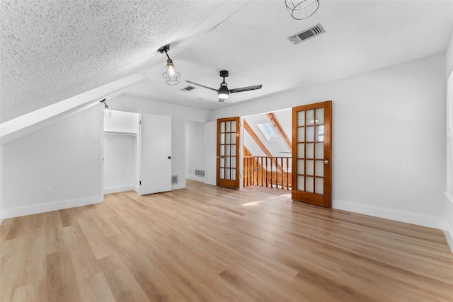 additional living space featuring ceiling fan, french doors, a textured ceiling, and light wood-type flooring