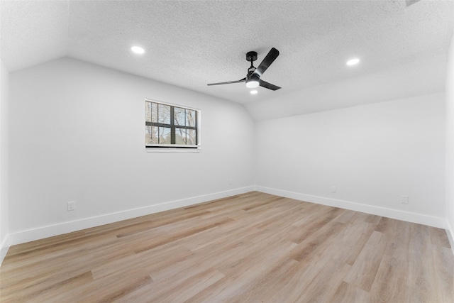 spare room featuring a textured ceiling, light hardwood / wood-style flooring, and vaulted ceiling