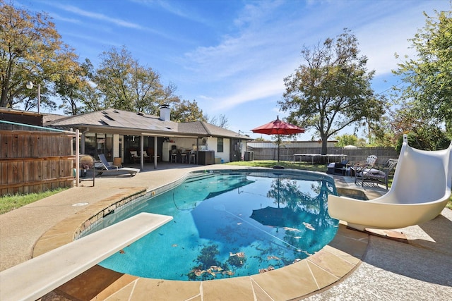 view of swimming pool featuring a water slide, a patio area, a fenced backyard, and a diving board