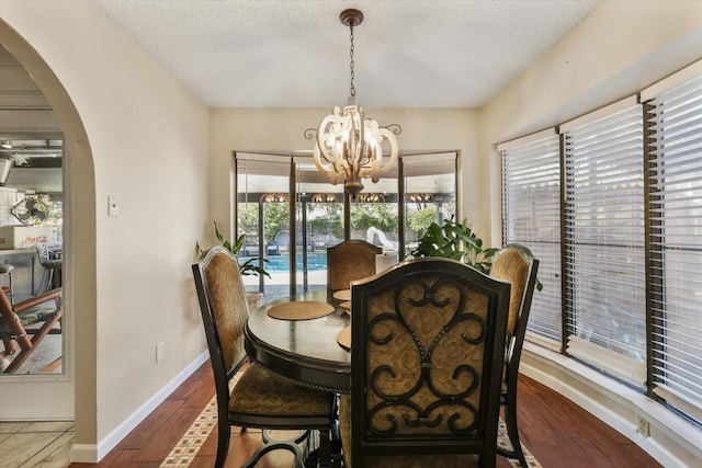 dining space with arched walkways, a chandelier, baseboards, dark wood-style flooring, and a textured ceiling
