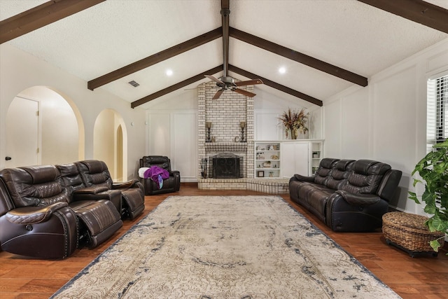 living room with wood finished floors, a decorative wall, a ceiling fan, a brick fireplace, and arched walkways