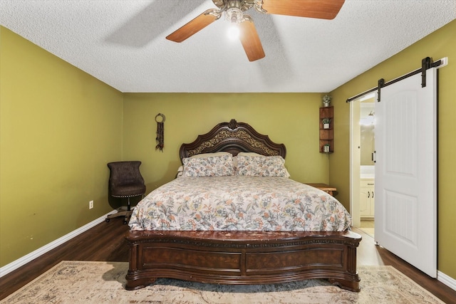 bedroom featuring dark wood-style floors, baseboards, a textured ceiling, and a barn door
