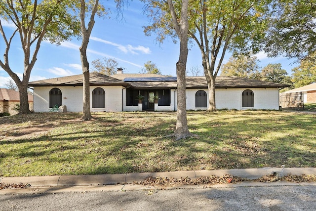 ranch-style house featuring brick siding, roof mounted solar panels, and a chimney