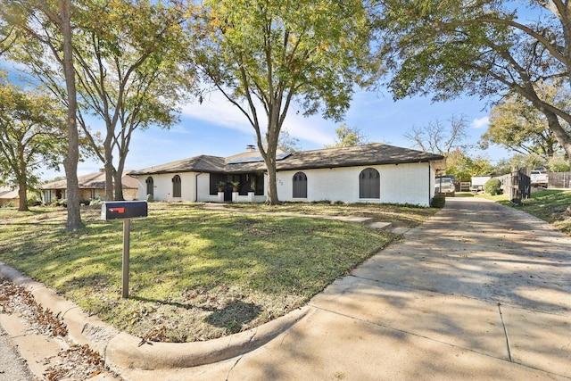 view of front of house featuring roof mounted solar panels, concrete driveway, a front yard, brick siding, and a chimney