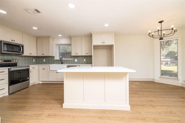 kitchen with hanging light fixtures, appliances with stainless steel finishes, light wood-type flooring, decorative backsplash, and a chandelier