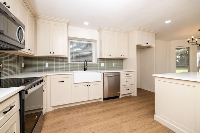 kitchen with appliances with stainless steel finishes, sink, backsplash, a notable chandelier, and light hardwood / wood-style flooring