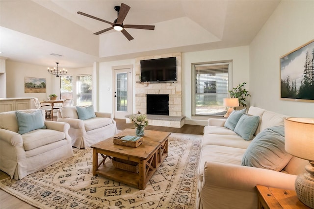 living room with ceiling fan with notable chandelier, a tray ceiling, light hardwood / wood-style flooring, and a fireplace