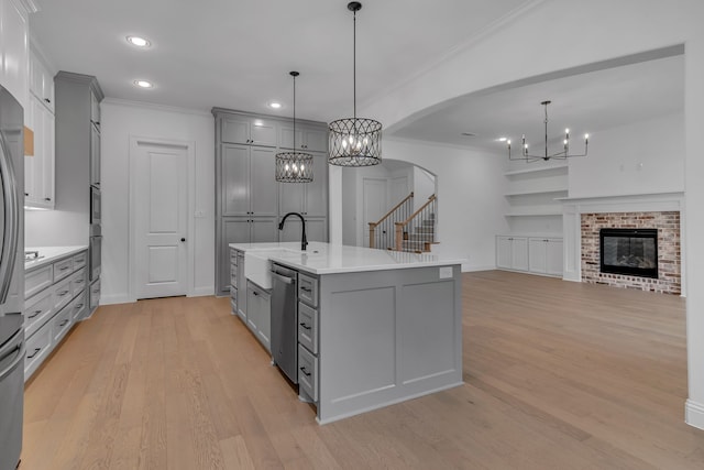 kitchen featuring light wood-type flooring, a kitchen island with sink, decorative light fixtures, a fireplace, and gray cabinets