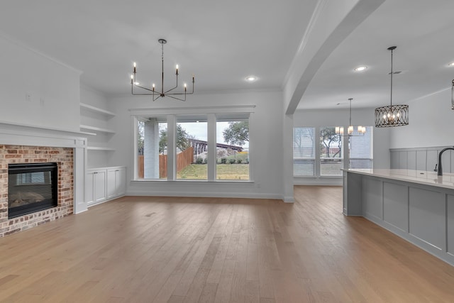 unfurnished living room with a chandelier, crown molding, a fireplace, and light hardwood / wood-style floors