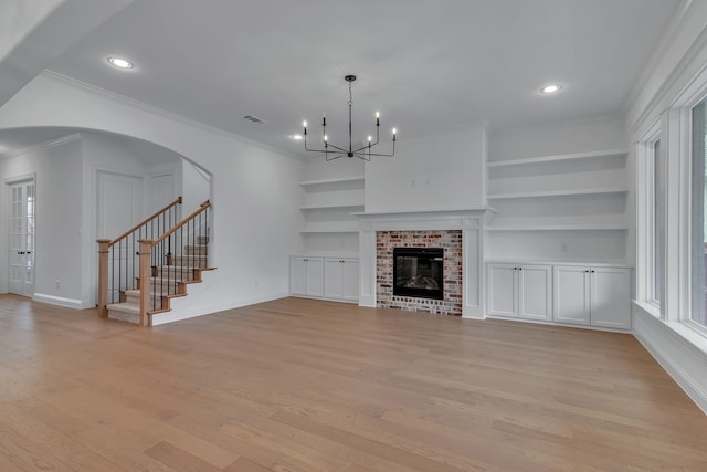 unfurnished living room featuring a fireplace, built in shelves, light hardwood / wood-style flooring, and crown molding