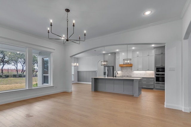 kitchen featuring a center island with sink, gray cabinets, hanging light fixtures, and appliances with stainless steel finishes