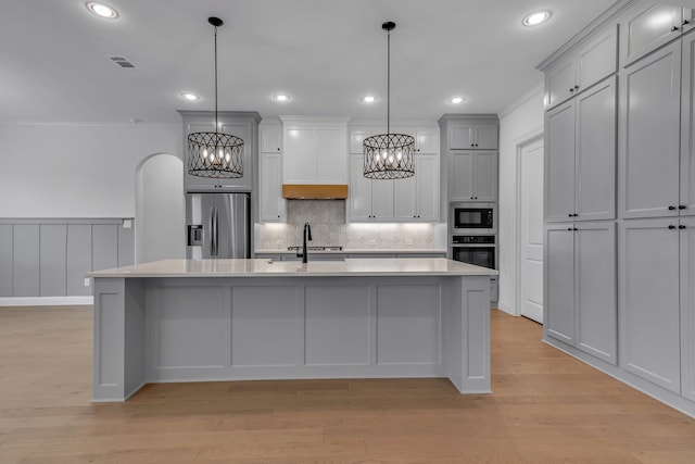 kitchen featuring an island with sink, stainless steel appliances, decorative light fixtures, and light wood-type flooring