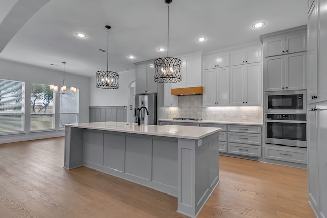 kitchen with appliances with stainless steel finishes, light hardwood / wood-style floors, a kitchen island with sink, and pendant lighting