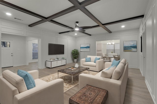 living room with beam ceiling, ceiling fan with notable chandelier, light hardwood / wood-style flooring, and coffered ceiling