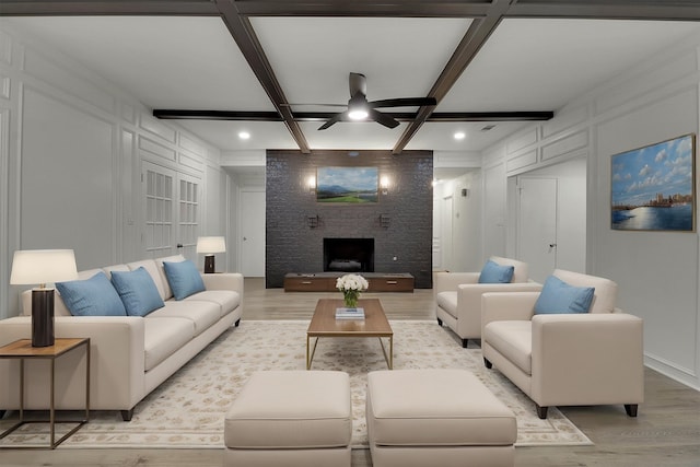 living room featuring coffered ceiling, light wood-type flooring, beamed ceiling, ceiling fan, and a fireplace