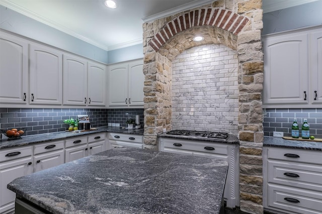 kitchen featuring decorative backsplash, white cabinetry, ornamental molding, and dark stone countertops