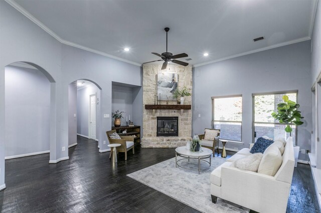 living room featuring ceiling fan, dark hardwood / wood-style flooring, a stone fireplace, and ornamental molding