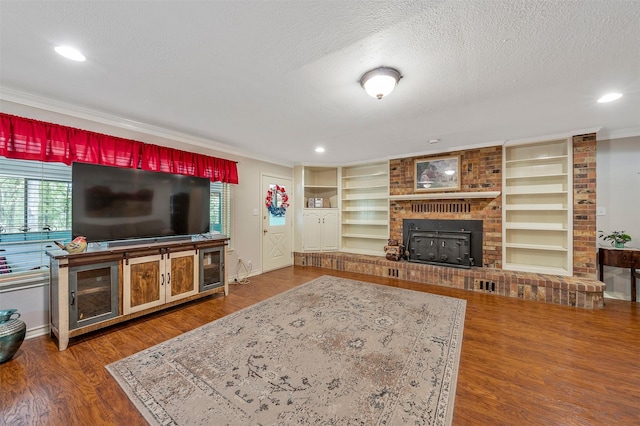 living room with built in shelves, a textured ceiling, ornamental molding, dark hardwood / wood-style floors, and a fireplace