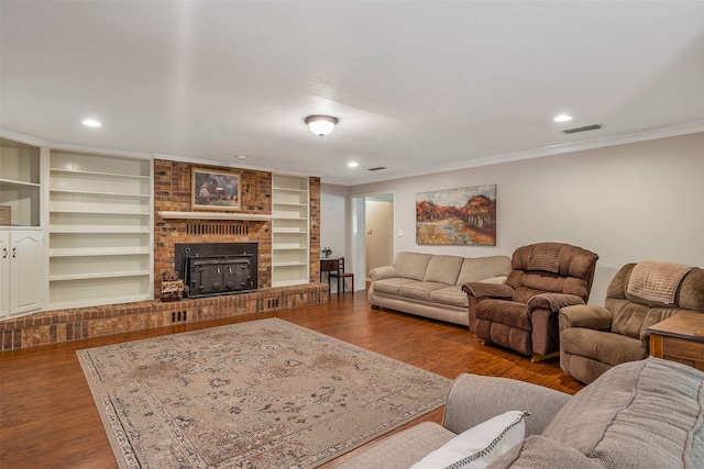 living room featuring a brick fireplace, crown molding, wood-type flooring, and built in shelves