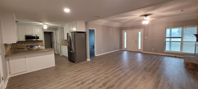 kitchen with light stone countertops, stainless steel appliances, backsplash, wood-type flooring, and white cabinets