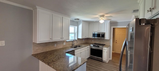 kitchen featuring kitchen peninsula, appliances with stainless steel finishes, sink, dark stone countertops, and white cabinets