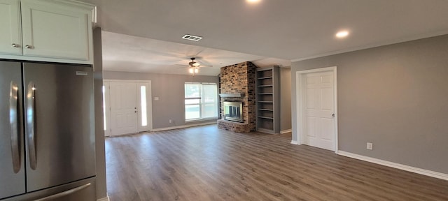 unfurnished living room featuring ceiling fan, hardwood / wood-style floors, ornamental molding, and a brick fireplace